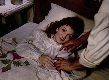 Movie still from “Drums Along the Mohawk” (1939), directed by John Ford – A woman laying in a bed next to a person touching her hand; Medium shot, Overhead angle