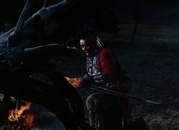 Movie still from “Drums Along the Mohawk” (1939), directed by John Ford – A man in a red jacket is lighting a fire; Wide shot, Over the shoulder angle