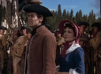 Movie still from “Drums Along the Mohawk” (1939), directed by John Ford – A man and a woman standing next to each other in front of a crowd; Medium shot, Low angle