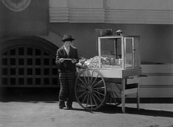 Movie still from “Duck Soup” (1933), directed by Leo McCarey – A man standing next to a cart of food on the street; Wide shot, High angle