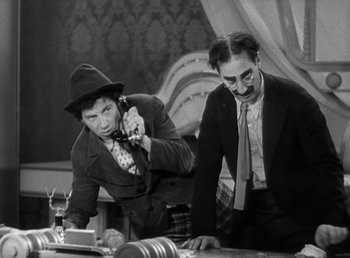 Movie still from “Duck Soup” (1933), directed by Leo McCarey – Two men are sitting at a table and one of them is on the phone; Medium shot, Low angle