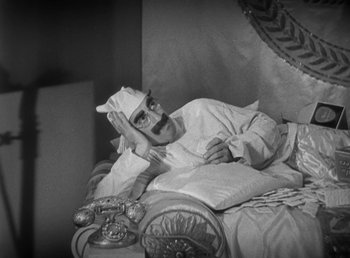 Movie still from “Duck Soup” (1933), directed by Leo McCarey – A man with a mustache and a beard is laying on a bed; Medium shot, High angle
