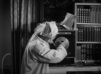 Movie still from “Duck Soup” (1933), directed by Leo McCarey – A man in a white lab coat and a mask is looking at a book; Medium shot, High angle