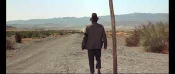 Movie still from “Duck, You Sucker!” (1971), directed by Sergio Leone – A man wearing a hat walking down a dirt road; Wide shot, Low angle