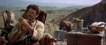 Movie still from “Duck, You Sucker!” (1971), directed by Sergio Leone – A man sitting in a chair next to a brown horse; Medium shot, Low angle