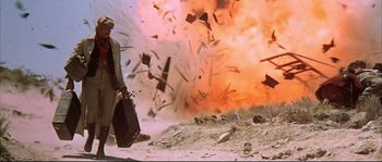 Movie still from “Duck, You Sucker!” (1971), directed by Sergio Leone – A man holding a suitcase walking in front of an explosion; Wide shot, Low angle