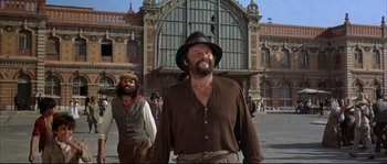 Movie still from “Duck, You Sucker!” (1971), directed by Sergio Leone – A man with a beard wearing a hat standing in front of a train station; Medium shot, Low angle