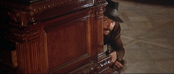 Movie still from “Duck, You Sucker!” (1971), directed by Sergio Leone – A man in a hat is peeking out from behind a wooden cabinet; Medium shot, Low angle