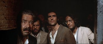 Movie still from “Duck, You Sucker!” (1971), directed by Sergio Leone – A group of men standing next to each other in a dark room; Medium shot, Low angle