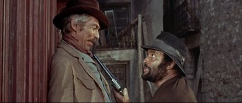 Movie still from “Duck, You Sucker!” (1971), directed by Sergio Leone – A man holding a gun and another man with a hat on; Medium shot, Over the shoulder angle