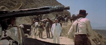 Movie still from “Duck, You Sucker!” (1971), directed by Sergio Leone – A group of men standing next to horses on a dirt road; Medium shot, Over the shoulder angle