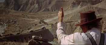 Movie still from “Duck, You Sucker!” (1971), directed by Sergio Leone – A man is reaching out his hand to a group of people in the desert; Wide shot, High angle