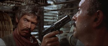 Movie still from “Duck, You Sucker!” (1971), directed by Sergio Leone – A man holding a gun up to his face in front of another man; Close Up shot, Over the shoulder angle