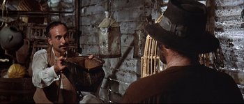 Movie still from “Duck, You Sucker!” (1971), directed by Sergio Leone – A man in a cowboy hat holding a basket in front of a wall; Medium shot, Over the shoulder angle