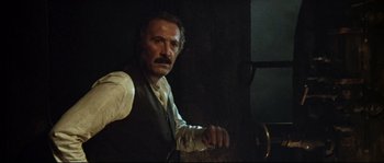 Movie still from “Duck, You Sucker!” (1971), directed by Sergio Leone – A man in a vest and tie sitting in front of a wall; Close Up shot, Low angle