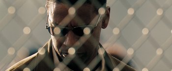 Movie still from “Deja Vu” (2006), directed by Tony Scott – A person wearing glasses behind a fence; Close Up shot, Low angle