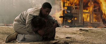 Movie still from “Deja Vu” (2006), directed by Tony Scott – A man kneeling on the ground holding a chicken in front of a burning building; Medium shot, Over the shoulder angle
