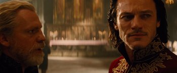 Movie still from “Dracula Untold” (2014), directed by Gary Shore – A man in a red and gold suit in a room; Close Up shot, Over the shoulder angle