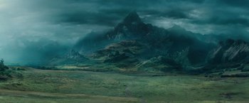 Movie still from “Dracula Untold” (2014), directed by Gary Shore – A green field with mountains in the background under a cloudy sky; Extreme Wide shot, High angle