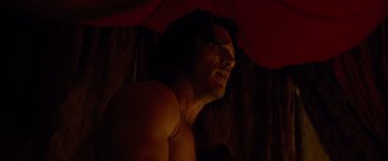 A shirtless man with long hair under an umbrella