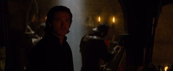 Movie still from “Dracula Untold” (2014), directed by Gary Shore – A man standing in a dark room next to candles; Medium shot, Over the shoulder angle