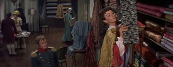 Movie still from “Désirée” (1954), directed by Henry Koster – A woman is standing in front of a mirror in a dress shop; Medium shot, Over the shoulder angle