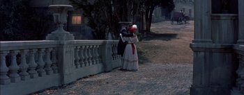 Movie still from “Désirée” (1954), directed by Henry Koster – A woman dressed in period clothing standing next to a fence; Wide shot, High angle
