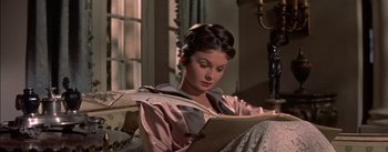 Movie still from “Désirée” (1954), directed by Henry Koster – A woman sitting in front of an open book in a room; Medium shot, High angle