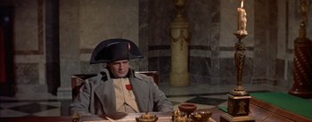 Movie still from “Désirée” (1954), directed by Henry Koster – A man sitting at a table with a hat on his head; Medium shot, High angle