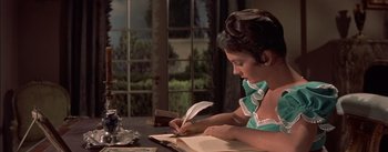 Movie still from “Désirée” (1954), directed by Henry Koster – A woman is writing on a book with a feather pen; Medium shot, High angle