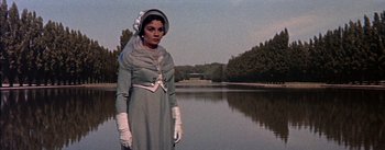 Movie still from “Désirée” (1954), directed by Henry Koster – A woman in a gray dress and white gloves standing in front of a body of water; Medium shot, Low angle