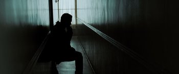 Movie still from “Eagle Eye” (2008), directed by D.J. Caruso – A man sitting on a bench in a dark room talking on a phone; Wide shot, Low angle