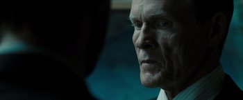 Movie still from “Eagle Eye” (2008), directed by D.J. Caruso – An older man looking into the camera with a serious look on his face; Close Up shot, Over the shoulder angle