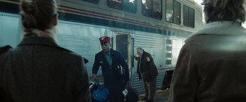 Movie still from “Eagle Eye” (2008), directed by D.J. Caruso – A man in a red hat is walking next to a train; Medium shot, Over the shoulder angle