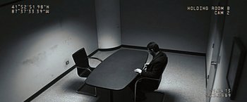 Movie still from “Eagle Eye” (2008), directed by D.J. Caruso – A man sitting at a table in front of two chairs; Wide shot, High angle