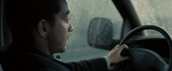 Movie still from “Eagle Eye” (2008), directed by D.J. Caruso – A man in a suit driving a car in the rain; Close Up shot, Over the shoulder angle