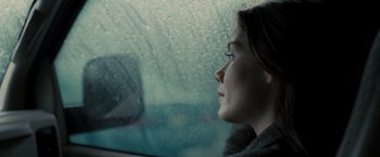 Movie still from “Eagle Eye” (2008), directed by D.J. Caruso – A woman sitting in the driver's seat of a car looking out the window; Close Up shot, Over the shoulder angle
