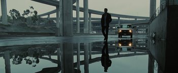 Movie still from “Eagle Eye” (2008), directed by D.J. Caruso – A man standing on the side of a road next to a bridge; Wide shot, Low angle