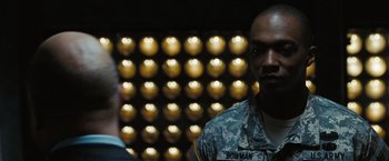 Movie still from “Eagle Eye” (2008), directed by D.J. Caruso – A man in a military fatigues standing in front of lights; Close Up shot, Over the shoulder angle