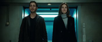 Movie still from “Eagle Eye” (2008), directed by D.J. Caruso – A man and a woman standing next to each other in front of an escalator; Medium shot, Low angle