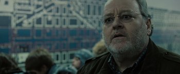 Movie still from “Eagle Eye” (2008), directed by D.J. Caruso – An older man with a beard wearing glasses and a jacket; Close Up shot, Over the shoulder angle