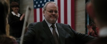 Movie still from “Eagle Eye” (2008), directed by D.J. Caruso – A man in a suit and tie in front of an american flag; Close Up shot, Low angle