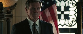 Movie still from “Eagle Eye” (2008), directed by D.J. Caruso – A man wearing a suit and tie in front of an american flag; Close Up shot, Low angle