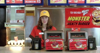 Movie still from “Eagle vs Shark” (2007), directed by Taika Waititi – A woman in a yellow hat is behind the counter of a fast - food restaurant; Medium shot, High angle