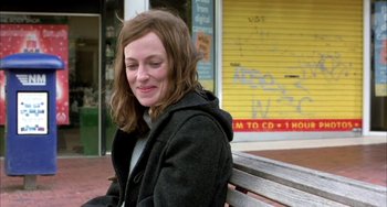 Movie still from “Eagle vs Shark” (2007), directed by Taika Waititi – A woman sitting on top of a wooden park bench; Medium shot, Over the shoulder angle