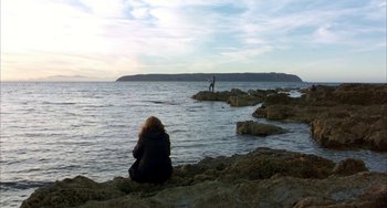 Movie still from “Eagle vs Shark” (2007), directed by Taika Waititi – A woman sitting on a rock looking out at the ocean; Extreme Wide shot, Low angle