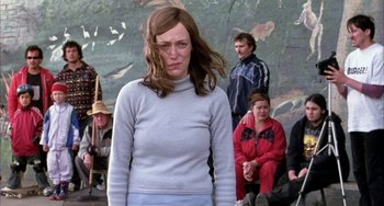 Movie still from “Eagle vs Shark” (2007), directed by Taika Waititi – A woman in a blue sweater standing in front of a group of people; Medium shot, Low angle