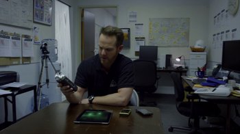Movie still from “Earth to Echo” (2014), directed by Dave Green – A man sitting at a table holding a cell phone; Medium shot, Overhead angle