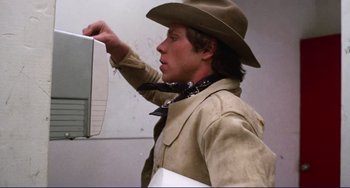 Movie still from “Eat My Dust” (1976), directed by Charles B. Griffith – A man wearing a cowboy hat holding a laptop; Close Up shot, Low angle