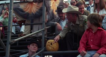 Movie still from “Eat My Dust” (1976), directed by Charles B. Griffith – A man that is holding a pumpkin; Medium shot, High angle